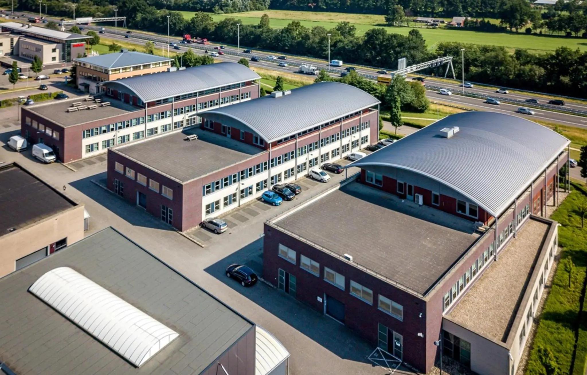 Luchtfoto van bedrijvencomplex De Wel met meerdere kantoorpanden langs een snelweg.